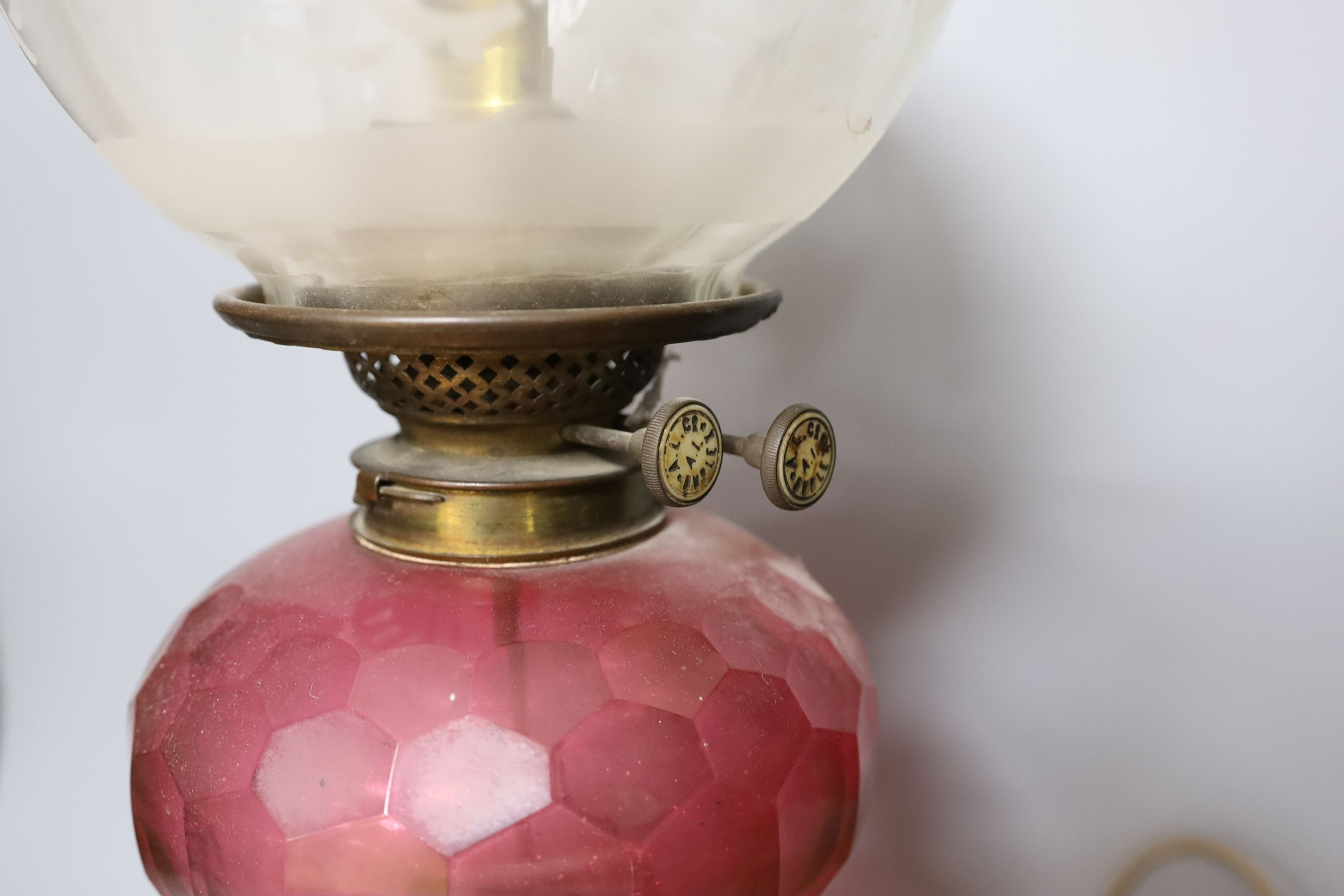 An Edwardian oil lamp with ruby glass font, later inverted to electricity, 57 cms high including funnel.